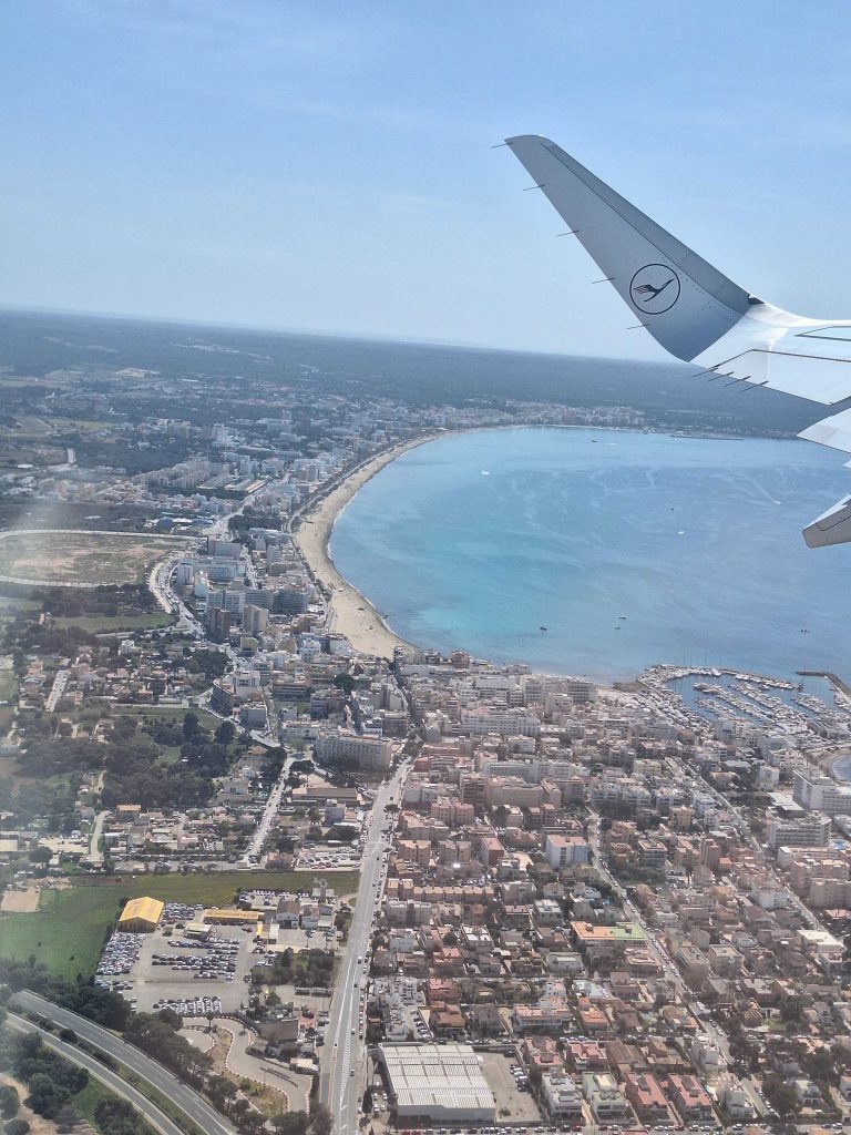 Blick aus dem Flugzeug auf Mallorca mit Strand und Stadt – Luftaufnahme bei der Landung auf panikontour.de