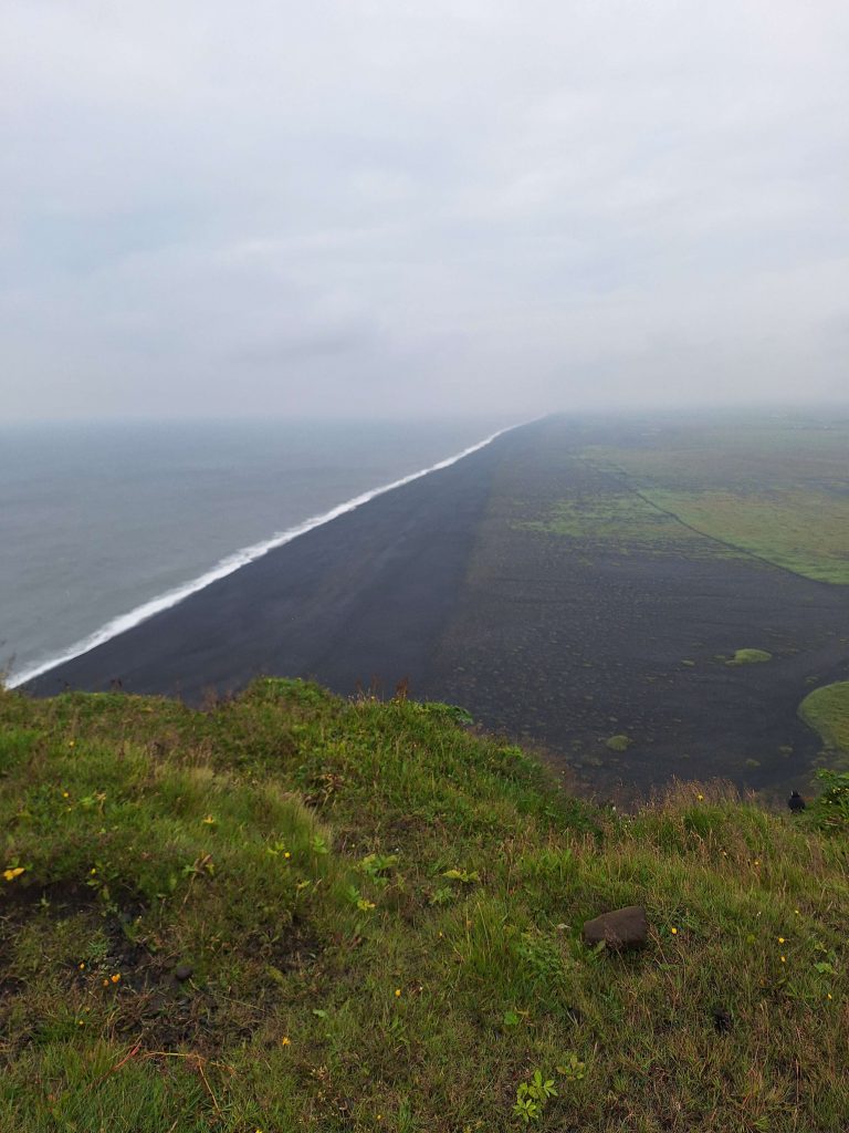 Schwarzer Sandstrand von Vík in Island mit grünem Küstenvorland und Nebel – Natur und Weite auf panikontour.de