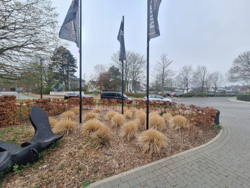 Ankerdenkmal mit Fahnen in Brunsbüttel – maritimer Platz mit Autos und Bäumen auf panikontour.de