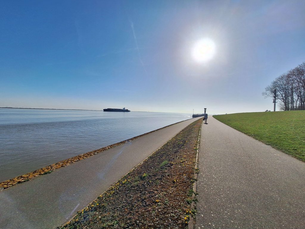 Spaziergang am Elbdeich bei Brunsbüttel mit Sonne und Frachtschiff – ruhige Wasserlandschaft auf panikontour.de