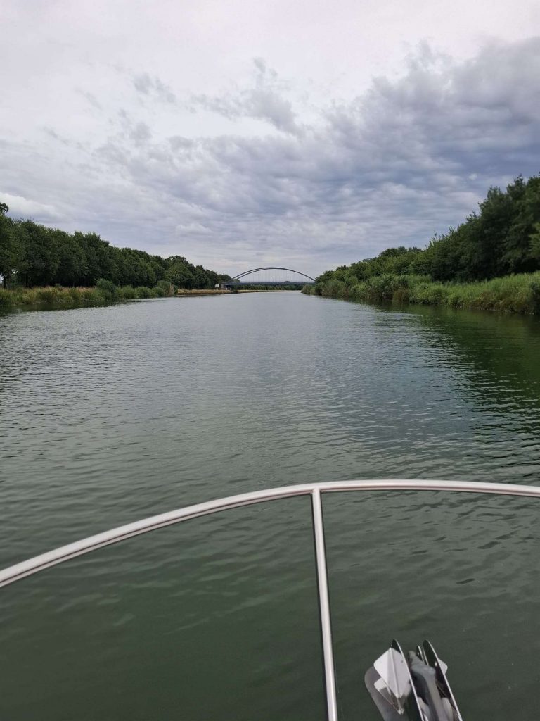 Bootsfahrt auf dem Kanal bei bewölktem Himmel – ruhige Wasserlandschaft mit Brücke im Hintergrund auf panikontour.de