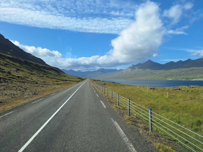 Leere Straße an Islands Ostküste mit Blick auf Meer, Berge und blauen Himmel