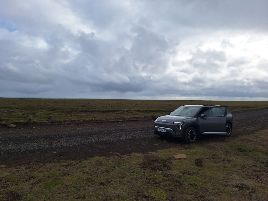 Auto auf isländischer Schotterstraße unter grauem Himmel