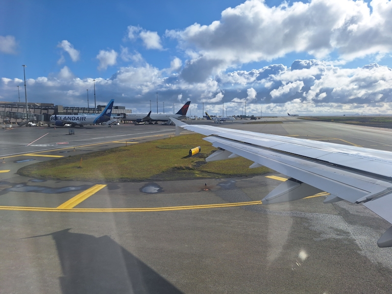Blick aus dem Flugzeugfenster auf Startbahn und Flugzeuge in Island